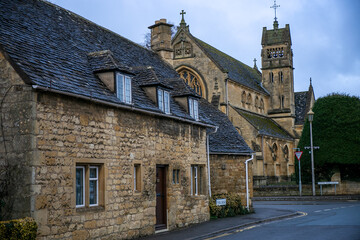 View of Park Road in Chipping Campden, featuring a charming Grade II listed stone cottage in the foreground. The scene provides a clear view towards St Catherine's Church in the background © Val