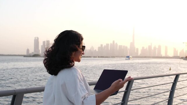 Woman working remotely on laptop outdoors with Dubai skyline background