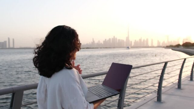 Female startup founder working remotely outdoors with laptop and Dubai skyline video