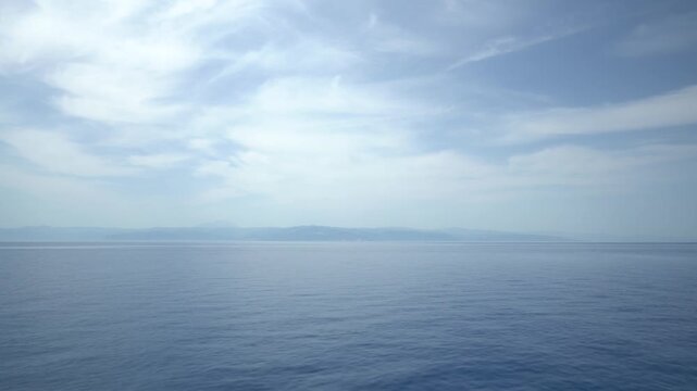 4K video of serene Sicilian seascape with calm Mediterranean waters, distant coastline, and soft cloudy sky. Peaceful ocean horizon view from Sicily, Italy.