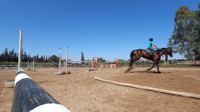 Close-up of a bay horse and rider jumping over a fence in an outdoor equestrian arena. The rider, dressed in black athletic gear and a helmet, demonstrates precise focus as the horse