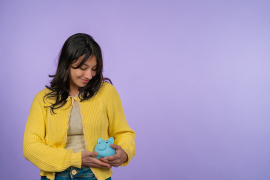 Young woman saving money holding blue piggy bank
