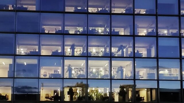 Business office building with full glass walls enlightened at night in Milan, Italy, with no people inside. 