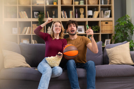 Couple watching basketball game on sofa cheering