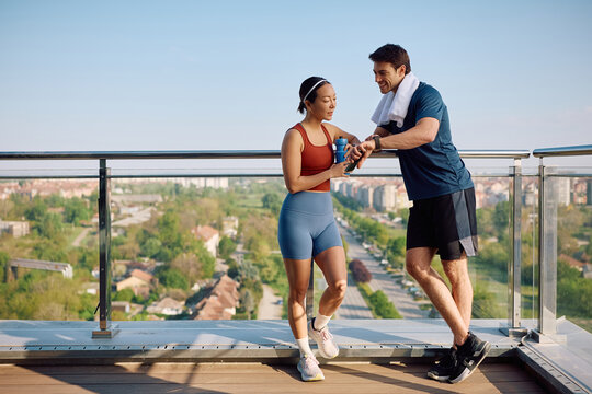 Athletic friends using fitness tracker while taking break from exercising on terrace.