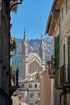Architectural spires of the historic Sant Bartomeu church framed by narrow old town street buildings in Soller Mallorca