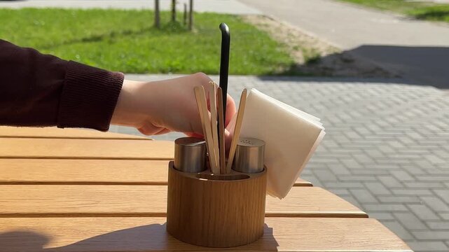 Waiter placing stack of white napkins into wooden table organizer at sunny outdoor restaurant close up service scene 