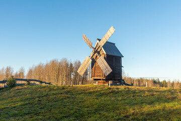 Fototapeta premium Wooden windmill on grassy hill under blue sky Museum of Wooden Architecture in Malye Karely, Arkhangelsk Region