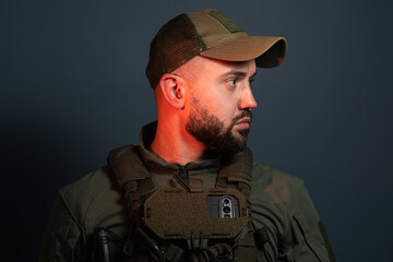 Obraz premium Bearded soldier wearing tactical uniform, cap, and plate carrier vest with chest-mounted chest rig smartphone navigation device looking away