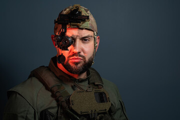Fototapeta premium Front view portrait of bearded soldier looking at camera, wearing tactical uniform and helmet with head-mounted night vision thermal monocular