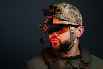 Profile portrait of bearded soldier wearing tactical uniform, tinted safety glasses, and helmet with head-mounted night vision thermal imaging device © Dmitri