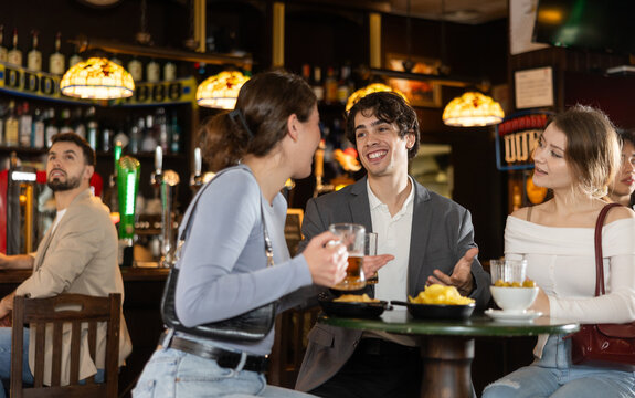 Lively conversation between friends. Youth girls and guys bar customer sitting at table, talking, laughing, joking, chatting, and spending time with friends. .