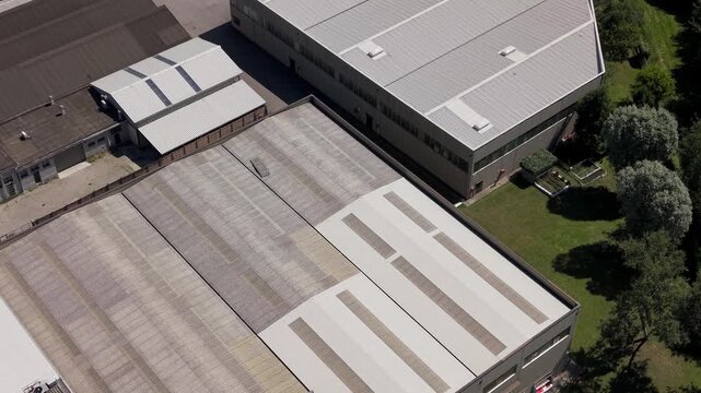 Industrial Rooftops: An aerial view captures the utilitarian design of industrial building rooftops, showcasing metallic surfaces and structural details against a backdrop of green trees and lawn.