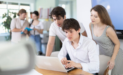 Fototapeta premium Several employees grouped around one laptop, heated discussion in office, process of discussion or discussion, discussion of work issues or news