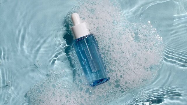 Bottle with a pipette for collagen serum, oil, toner on water texture background surface with bubbles of white soapy foam. Medical skin care. Packaging for design, advertising of a cosmetic product.4k