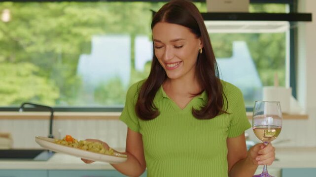 Happy young woman sitting at table with pasta and glass of wine, 4K slow motion