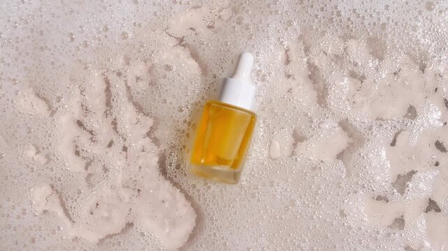 Bottle with a pipette for collagen serum, oil, toner on water texture background surface with bubbles of white soapy foam. Medical skin care. Packaging for design, advertising of a cosmetic product.4k