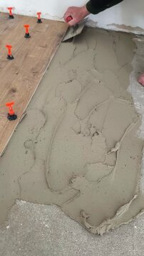A builder applies tile adhesive to a concrete floor using a notched trowel.
