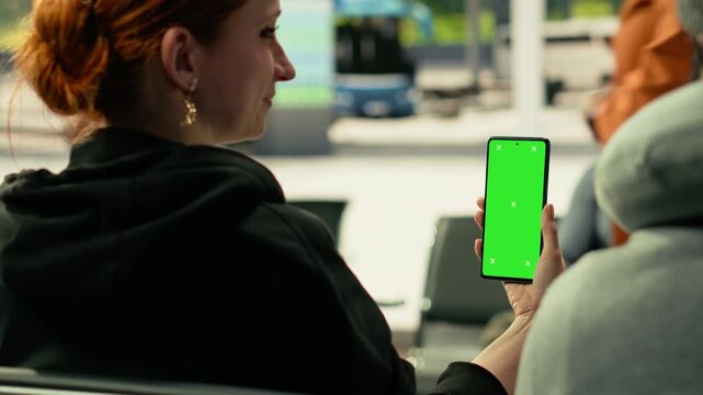 Vertical chroma key on smartphone held by black man waiting at metropolitan bus stop. Public transportation commuters and passengers move through the station, human flow urban energy.