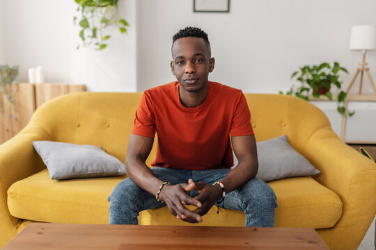 Confident African man sitting on sofa looking directly at the camera with a serious and thoughtful expression.