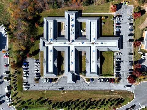 Aerial top-down drone view of symmetrical cross-shaped commercial office building complex in Daleville, Virginia surrounded by parking lots and autumn foliage