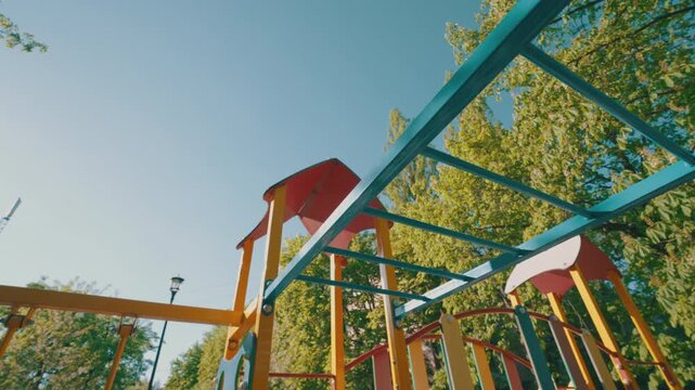 Colorful Monkey Bars on Children Playground | Wide-Angle Bottom-Up View | Urban Park Play Equipment Against Blue Sky and Green Trees