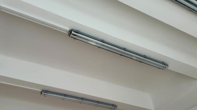 Fluorescent lamps hanging from studio ceiling, cool white tubes mounted between exposed beams creating minimalist industrial