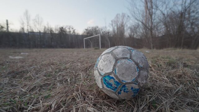 Old Worn Soccer Ball on Abandoned Overgrown Football Field | Wide-Angle Ground-Level View | Urban Decay, Neglect and Forgotten Sports Concept