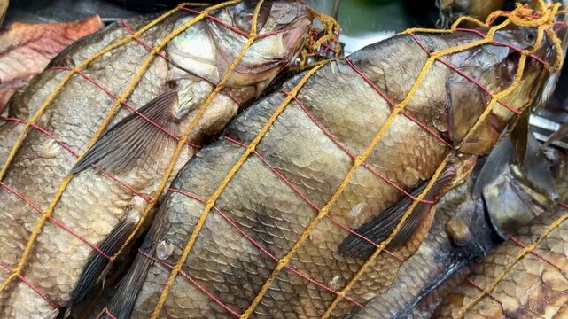 Cold smoked bream and walleye closeup, golden netting and textured scales on retail shelves, deli vendor arranging preserved fish