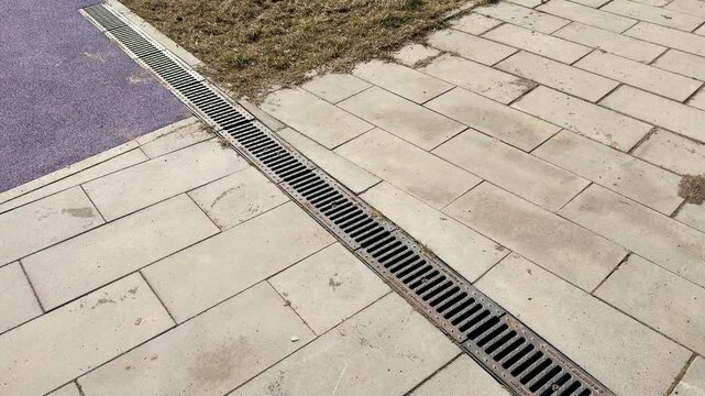 Overhead view metal drain channel sports field iron plate with holes for rainwater drainage, concrete paving meets purple turf
