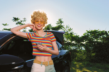 Fototapeta premium Cheerful woman outdoors, smiling beside a car, striped crop top, soft sunlight and relaxed casual vibe, retro fashion colors, lush greenery, sunny summer moment