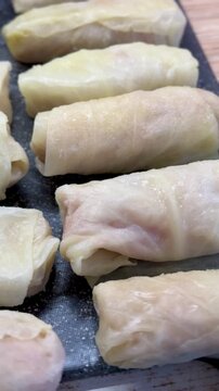 Cabbage rolls on black cutting board closeup, uncooked meat filled cabbage leaves rolled into neat cylinders, arranged in rows