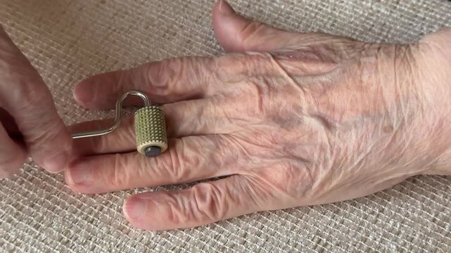 Elderly woman hand close-up rolling silver massager, textured roller with sharp edges gliding over wrinkled skin and knuckles