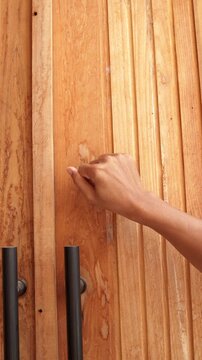 Close-up of a man's hand knocking on a modern door panel with a silver handle.