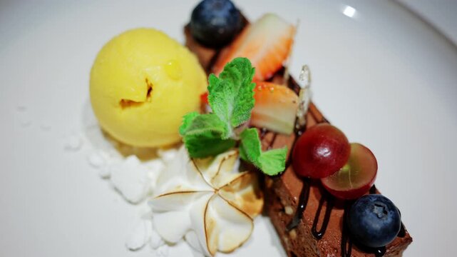 Close up of an elegant dessert served at a restaurant, featuring berries, cream, mint, chocolate, and a scoop of yellow sorbet
