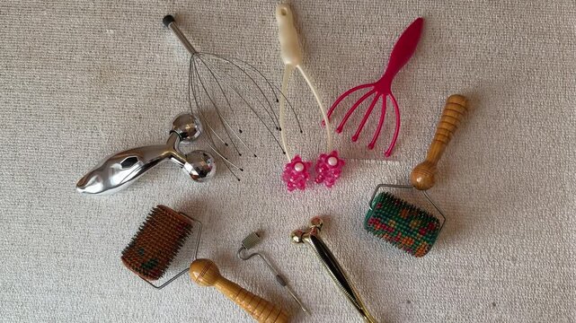 Assorted facial and head massagers arranged on neutral towel in treatment room, wooden roller, metal three ball massager, pink