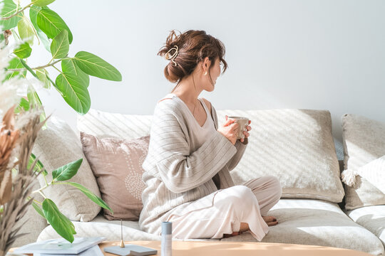 ソファーに座りホットドリンクを飲むおしゃれな女性