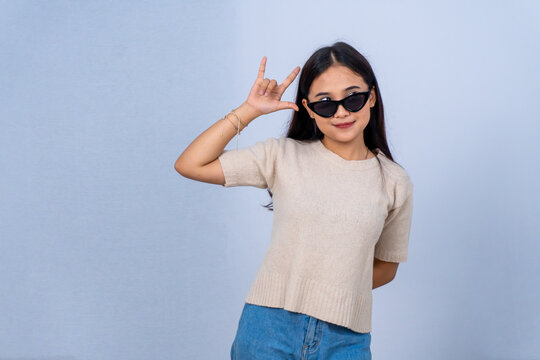 Cool Asian girl in sunglasses making ILY hand sign on blue background