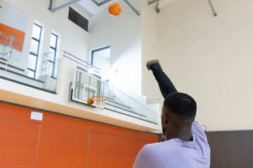 Fototapeta premium Basketball arcing toward hoop and glass backboard in gymnasium with mezzanine and skylight