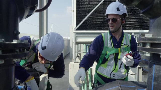 Engineer maintenance hvac cooling tower rooftop technician safety helmet harness on duty inspection and repair, adjust valve, radio, guide crew, manage pump test and service under bright sun