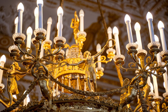 Magnificent ornate golden chandelier with white candle hanging from decorated baroque ceiling in opulent classical interior, luxury heritage concept.