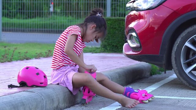 Little girl sitting on the curb putting on roller skates, preparing to skate outdoors.