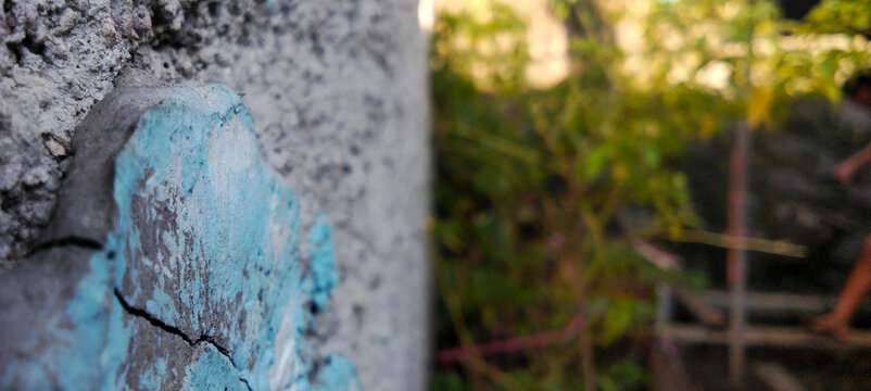 Close up of blue paint cracks on a concrete wall against a natural blurry background.