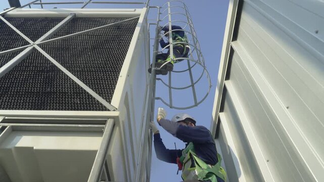Engineer maintenance hvac cooling tower ladder safety rooftop technician inspection, preventive maintenance on rooftop, caged ladder climb with safety harness and hard hat, operation under clear sky