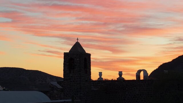 Witness stunning aerial views of Santa Rosalia Mission in Mulege with palm trees and mountains near the Sea of Cortez at sunset.