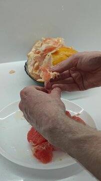 Detailed view of a person's hands carefully segmenting a ripe, red grapefruit, removing the bitter white pith and arranging the bright, succulent fruit pieces onto a pristine white plate, showcasing