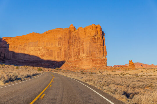 Asphalt road leads toward the massive red sandstone rock formation.