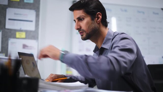 A busy businessman handles document work and takes a smartphone call in a messy office while feeling overworked