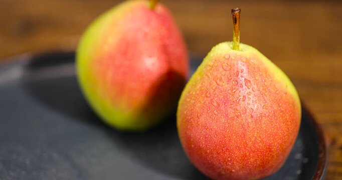 wet green-red ripe pears on a blue ceramic bowl on the table, several ripe hard and juicy pears are lying on a bowl on the kitchen table, the pears are covered with drops of water