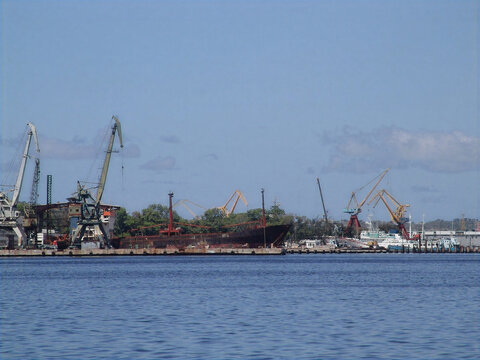 Cargo ship and industrial cranes at the port of Havana Cuba under a blue sky.